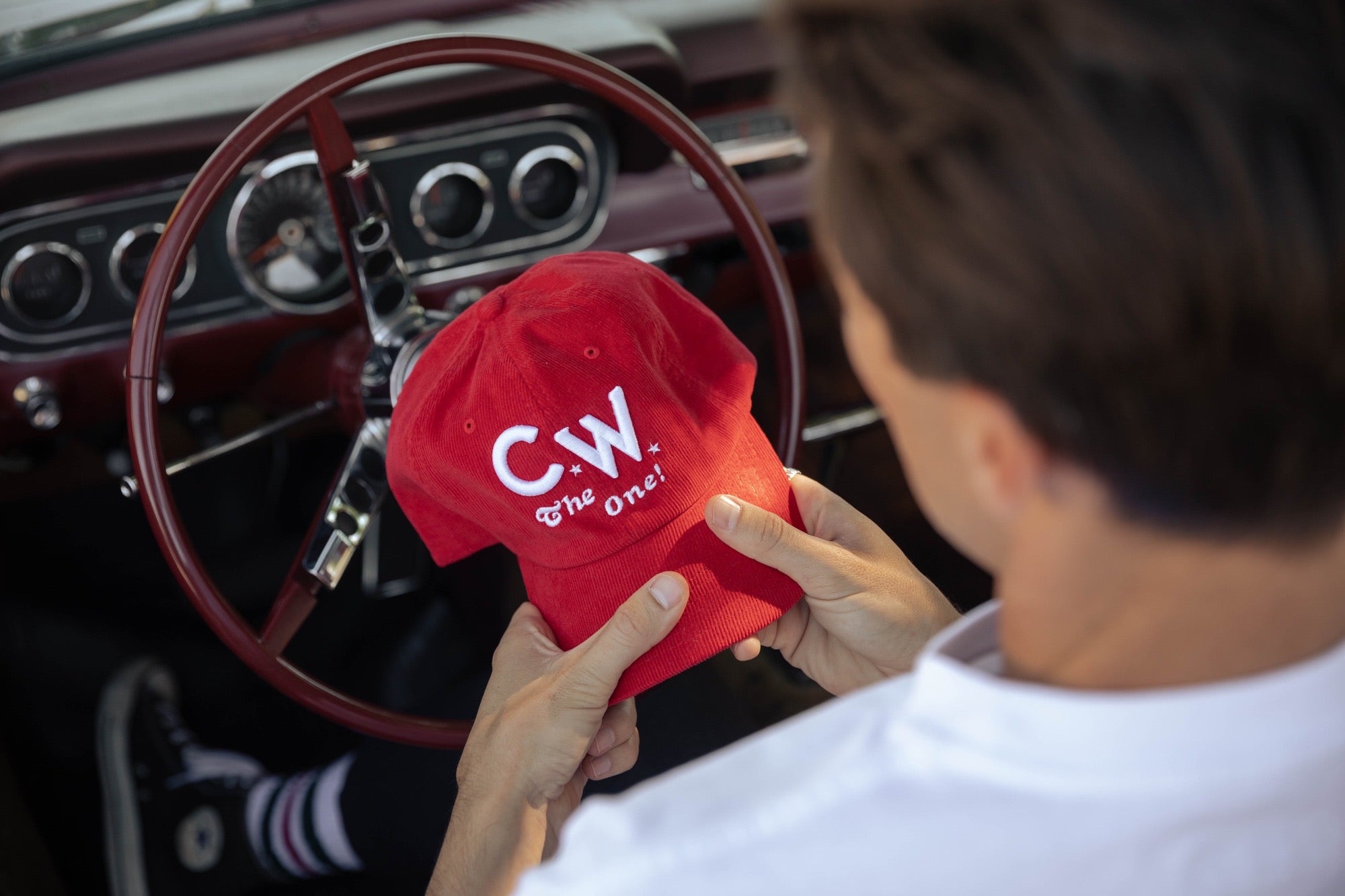 Man in car behind steering wheel holding red Curly Wolf Piston Cap