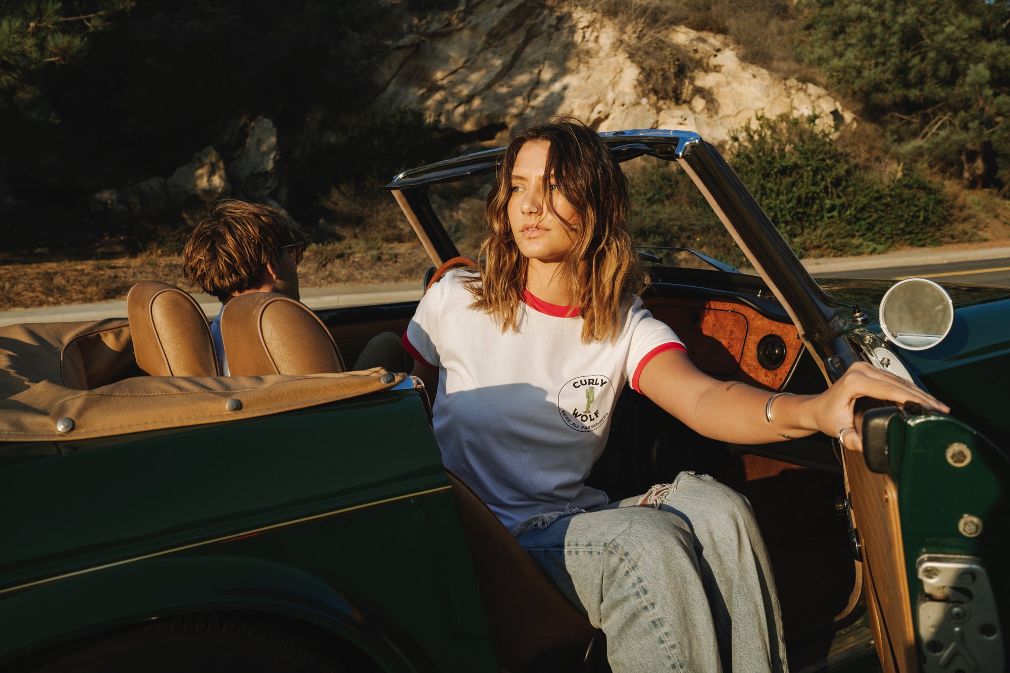 Woman stepping out of the passenger site of a green convertible car while wearing the Curly Wolf Tour Tee