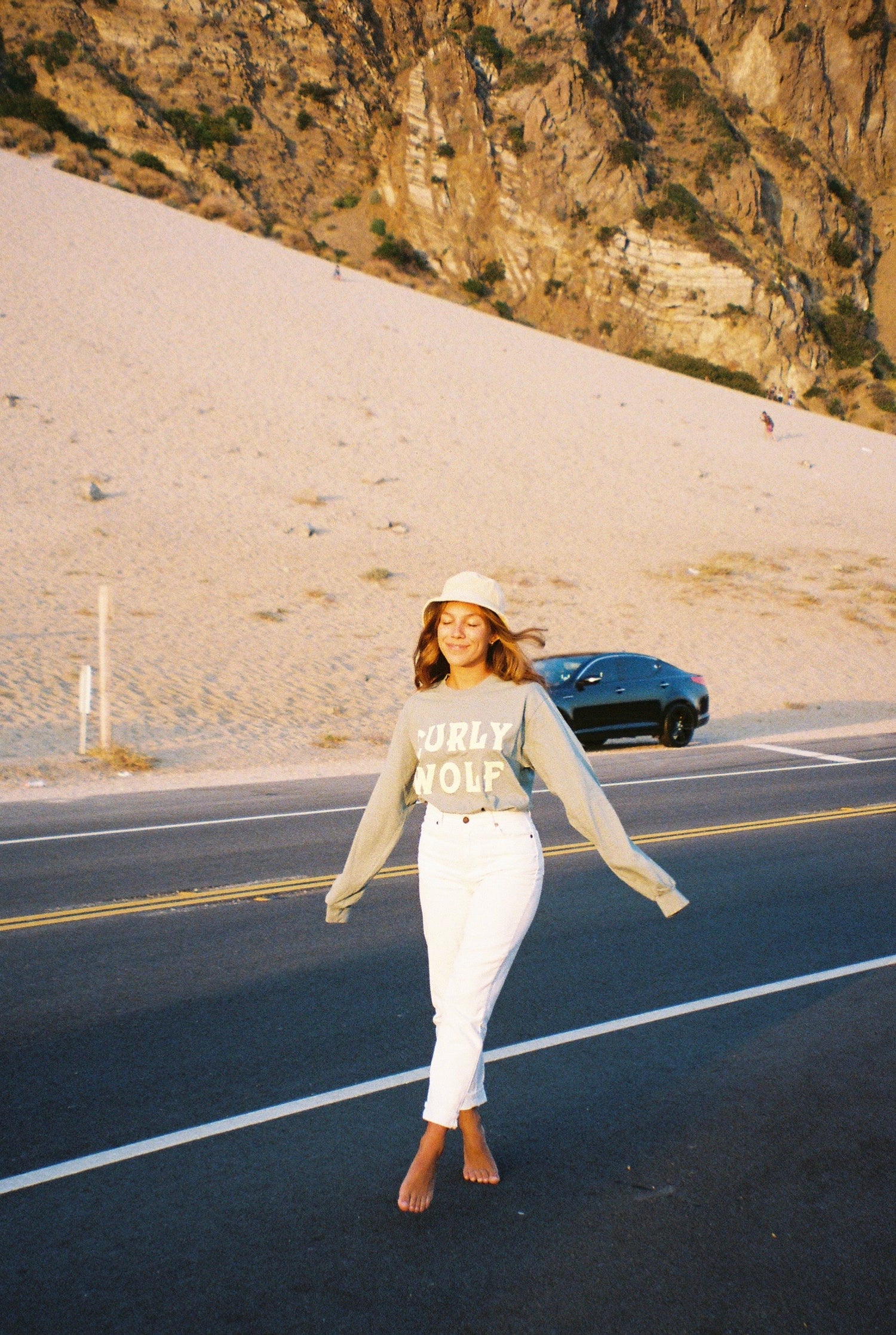 Woman walking in the street wearing a long sleeved cream shirt reading “CURLY WOLF”