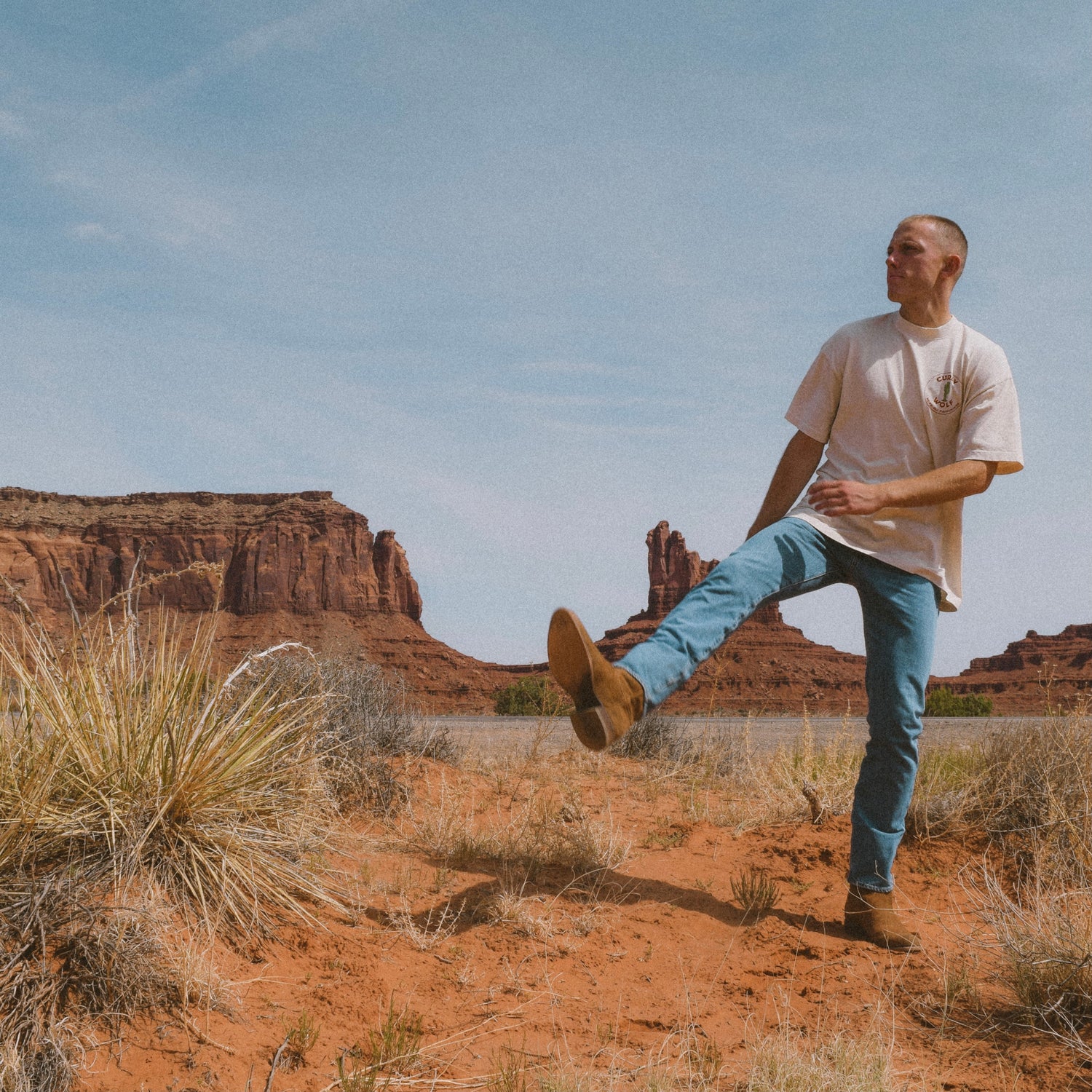 Man in desert wearing cowboy boots, jeans and Curly Wolf white t-shirt