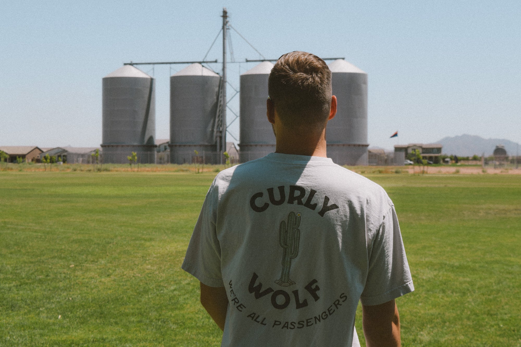 Man standing in a field with back towards camera. Shirt reads “CURLY WOLF”